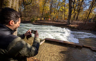 Freizeitsurfer Alexander Neumann fotografiert die - zurzeit nicht funktionstüchtige - Eisbachwelle im Englischen Garten. — © Peter Kneffel/dpa