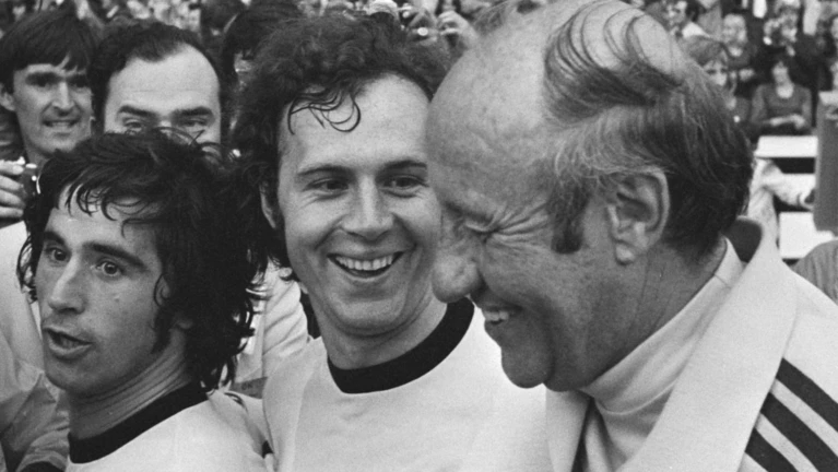 — © Von Bert Verhoeff für Anefo - Finale wereldkampioenschap voetbal 1974 in Munchen, West Duitsland tegen Nederland 2-1; v.l.n.r. Muller, Beckenbauer en trainer Schon na afloopDutch National Archives, The Hague, Fotocollectie Algemeen Nederlands Persbureau (ANeFo), 1945-1989,Auteursrechthebbende Nationaal Archief CC-BY-SA, Nummer toegang 2.24.01.05 Bestanddeelnummer 927-3108, CC BY-SA 3.0 nl, https://commons.wikimedia.org/w/index.php?curid=22812365