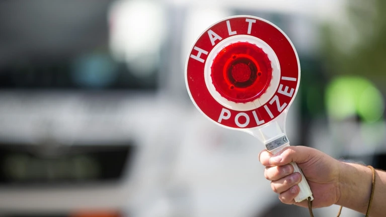 Ein Polizist hält bei einer Verkehrskontrolle eine Polizeikelle in der Hand. — © Jonas Güttler/dpa/Symbolbild