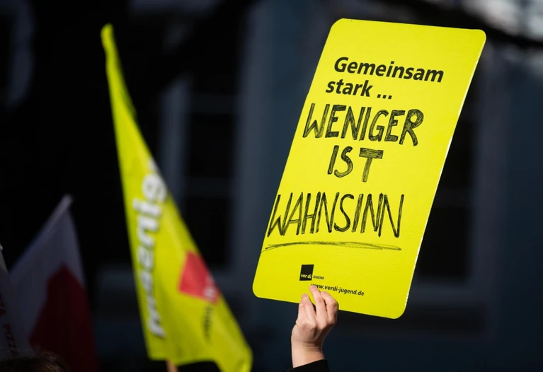 Warnstreiks, öffentlicher Dienst — © Bei einer Demonstration hält ein Mann ein Plakat mit der Aufschrift "Gemeinsam stark ... weniger ist Wahnsinn" in die Höhe. Foto: Nicolas Armer