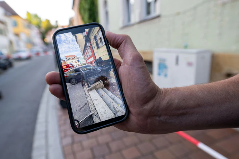 Der Hausbesitzer zeigt auf seinem Handy das Bild von dem Auto, das in der Hauswand steckt. — © Pia Bayer/dpa