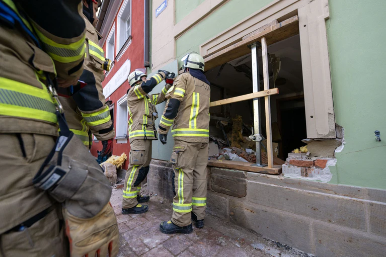 Einsatzkräfte der Feuerwehr sichern die Wand, in der ein großes Loch klafft. — © Pia Bayer/dpa