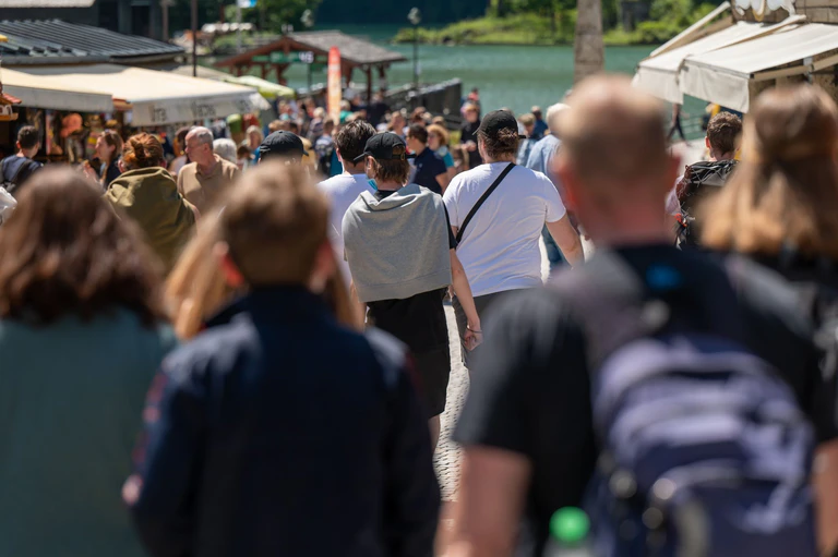 Touristen laufen eine Strasse zum Königssee hinunter. (Archivbild) — © Peter Kneffel/dpa