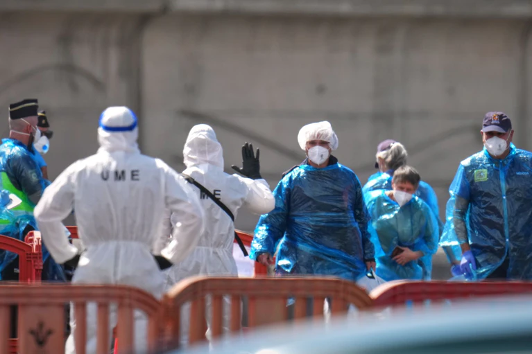 Personen in Schutzbekleidung und mit Masken (r) gehen im Hafen von Granadilla auf Teneriffa an Land, nachdem sie mit einem Boot von dem vom Hantavirus betroffenen Kreuzfahrtschiff MV Hondius gebracht wurden — © Manu Fernandez/AP/dpa