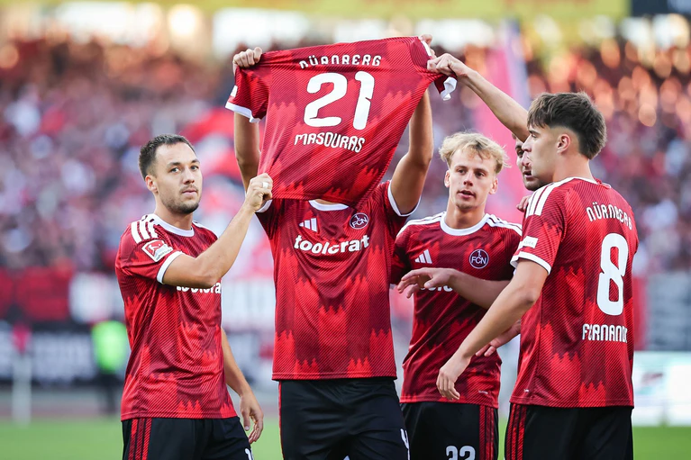 Besonderer Torjubel: Nach dem 1:0 halten Nürnbergs Profis das Trikot des fehlenden Kollegen Ioannis Masouras in die Höhe. — © Daniel Karmann/dpa
