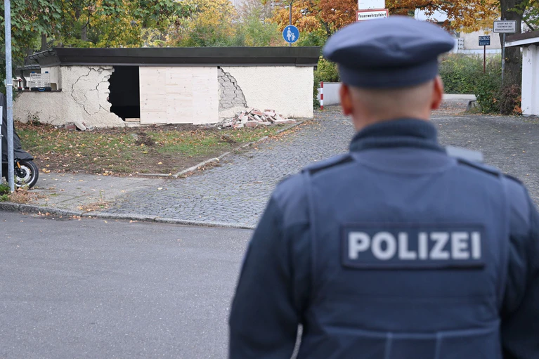 Ein Polizist betrachtet die beschädigte Garagenwand. — © Felix Hörhager/dpa