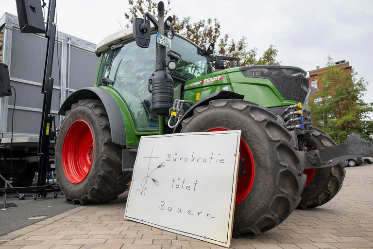 «Bürokratie tötet Bauern» steht auf einem Schild vor einem Traktor bei einer Kundgebung am Rande der Agrarministerkonferenz. — © Heiko Becker/dpa